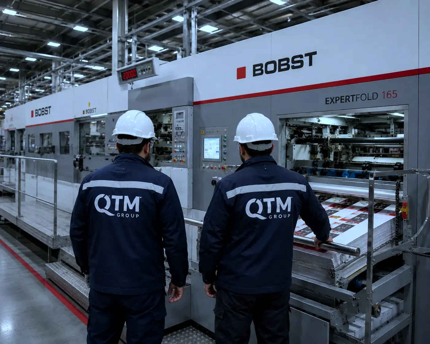 QTM Group specialists wearing protective hard hats at a BOBST packaging and printing line